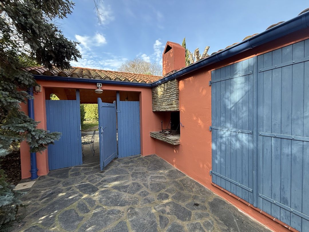 Cour de maison à Saint-Cyprien : murs extérieurs repeints en terracotta autour du barbecue, portail et volets bleus