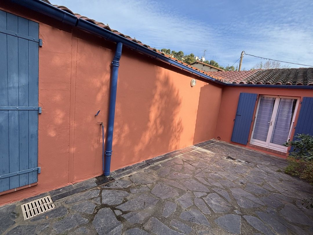 Façade de maison repeinte en terracotta par Duflot Peinture à Saint-Cyprien, volets et gouttières bleus, cour en pierre